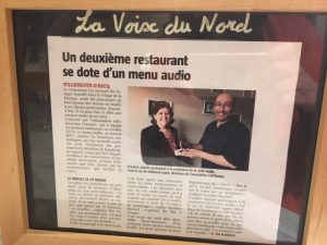 Article dans le restaurant expliquant l'accessibilité aux non-voyants au menu du restaurant et citant le soutien de FabAccess